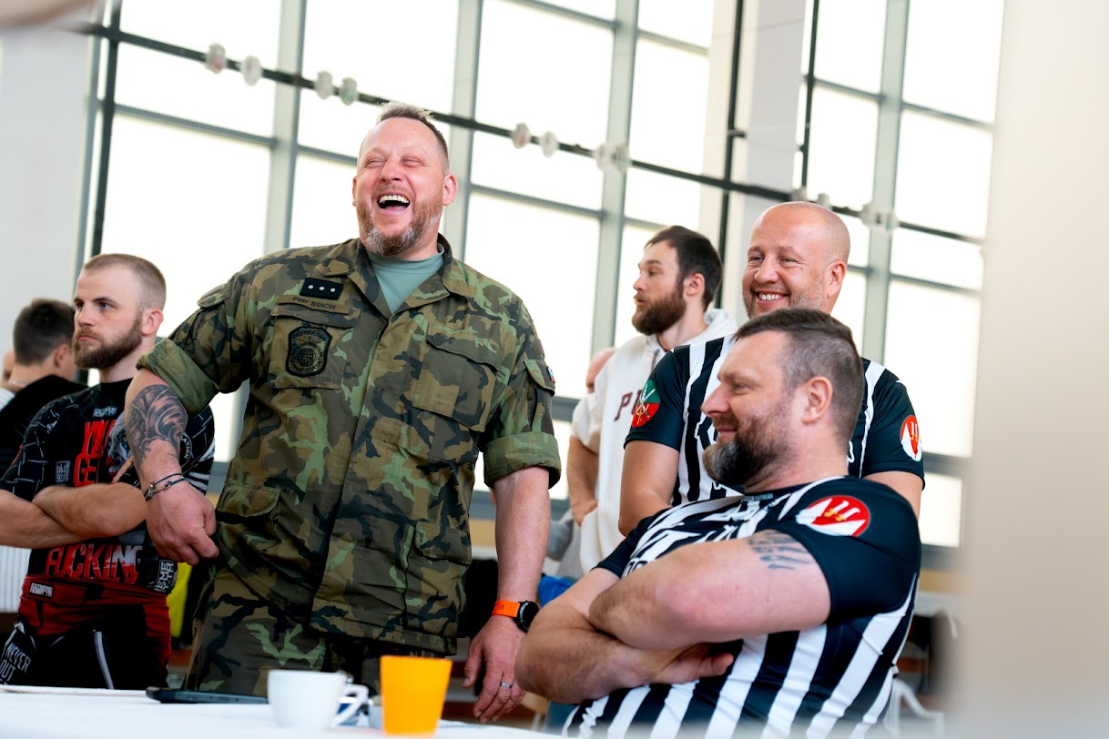 Voják v maskovací uniformě a rozhodčí v pruhovaných tričkách ve sportovní hale.