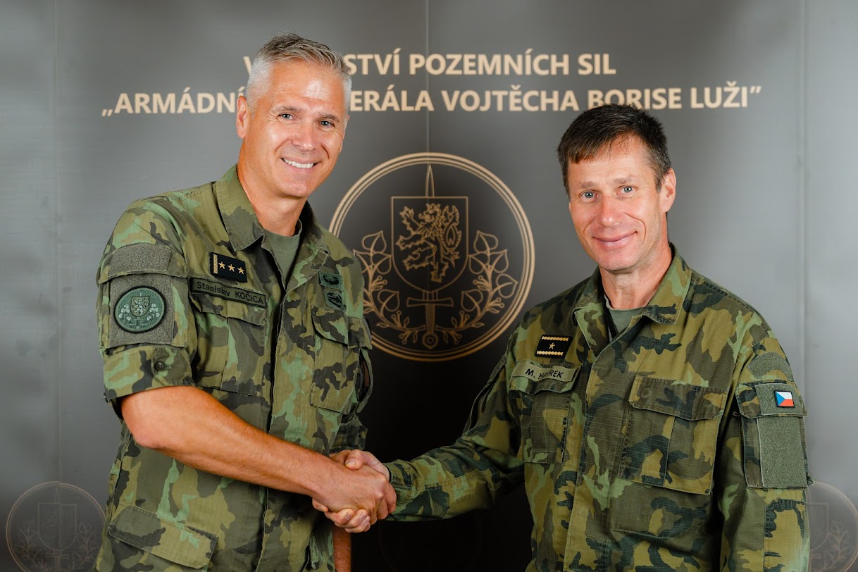 Dva vojáci v maskovacích uniformách si podávají ruce před označením Velitelství pozemních sil.