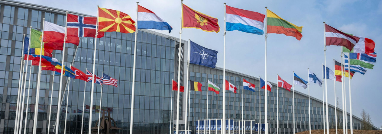 Sídlo NATO v Bruselu s vlajkami členských států. Kolektivní obrana Aliance stojí na jednotě, připravenosti a společném postupu spojenců.