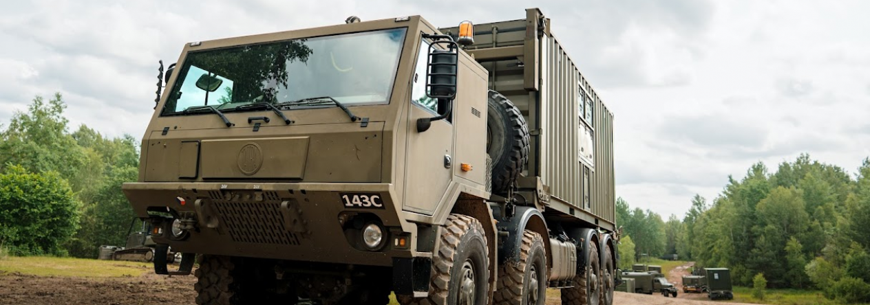 Tatra 815-7 8×8 v provedení hákového nakladače při přepravě kontejneru v terénu.
