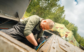 Voják na korbě pásového vozidla kontroluje technický stav během výcviku