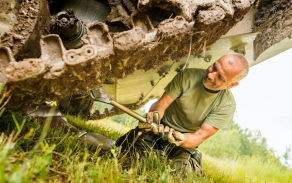 Mechanik pracuje pod pásovým vozidlem při odstraňování závady přímo v prostoru výcviku.